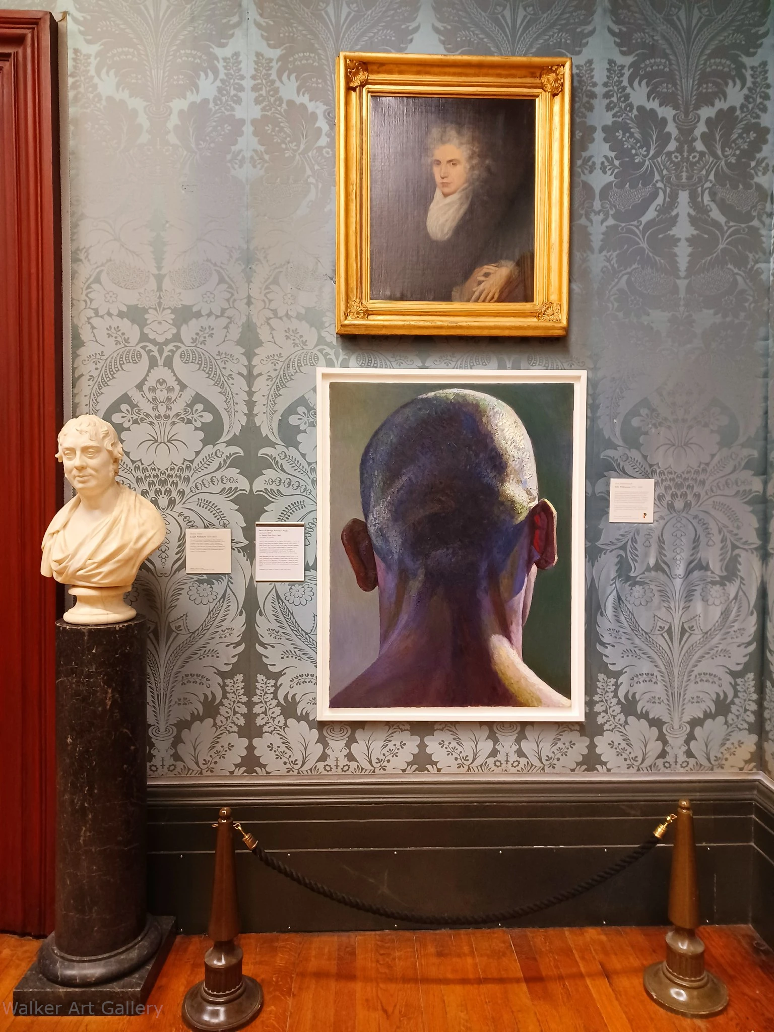 Detailed fine art painting in an art gallery. Painting illustrates the back of someone's head. Painting is next to a beautiful statue.