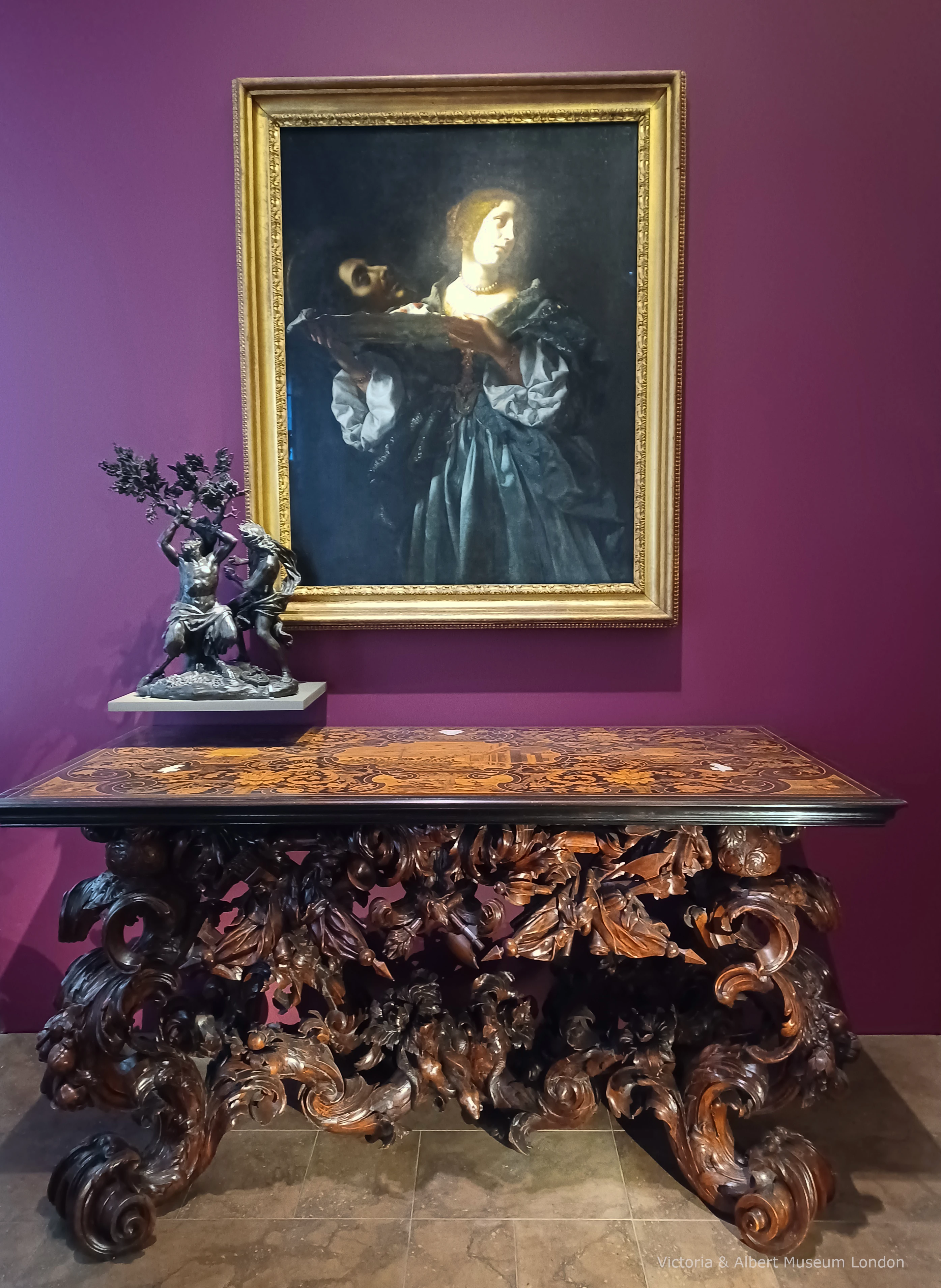Art gallery scene showing beautiful large wooden table with thick legs that have been carved to look like various plants and flowers.