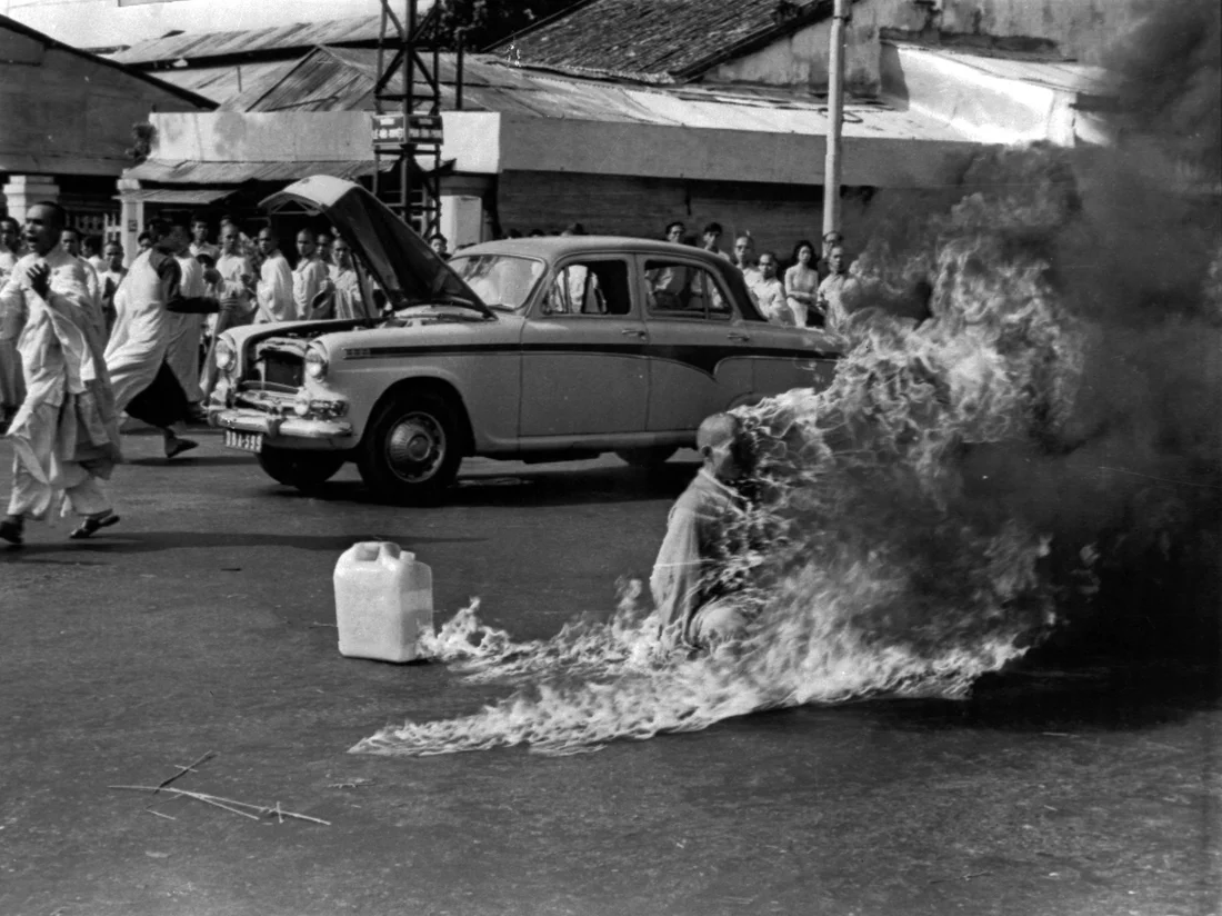 Horrifying photograph shows a buddhist monnk sitting on the floor engulfed in flames. Next to him there is a big can of petrol. The photo is black and white. This powerful image, taken on June 11, 1963, depicts the self-immolation of Vietnamese monk Thích Quảng Đức in Saigon, capturing a haunting and poignant moment in history.