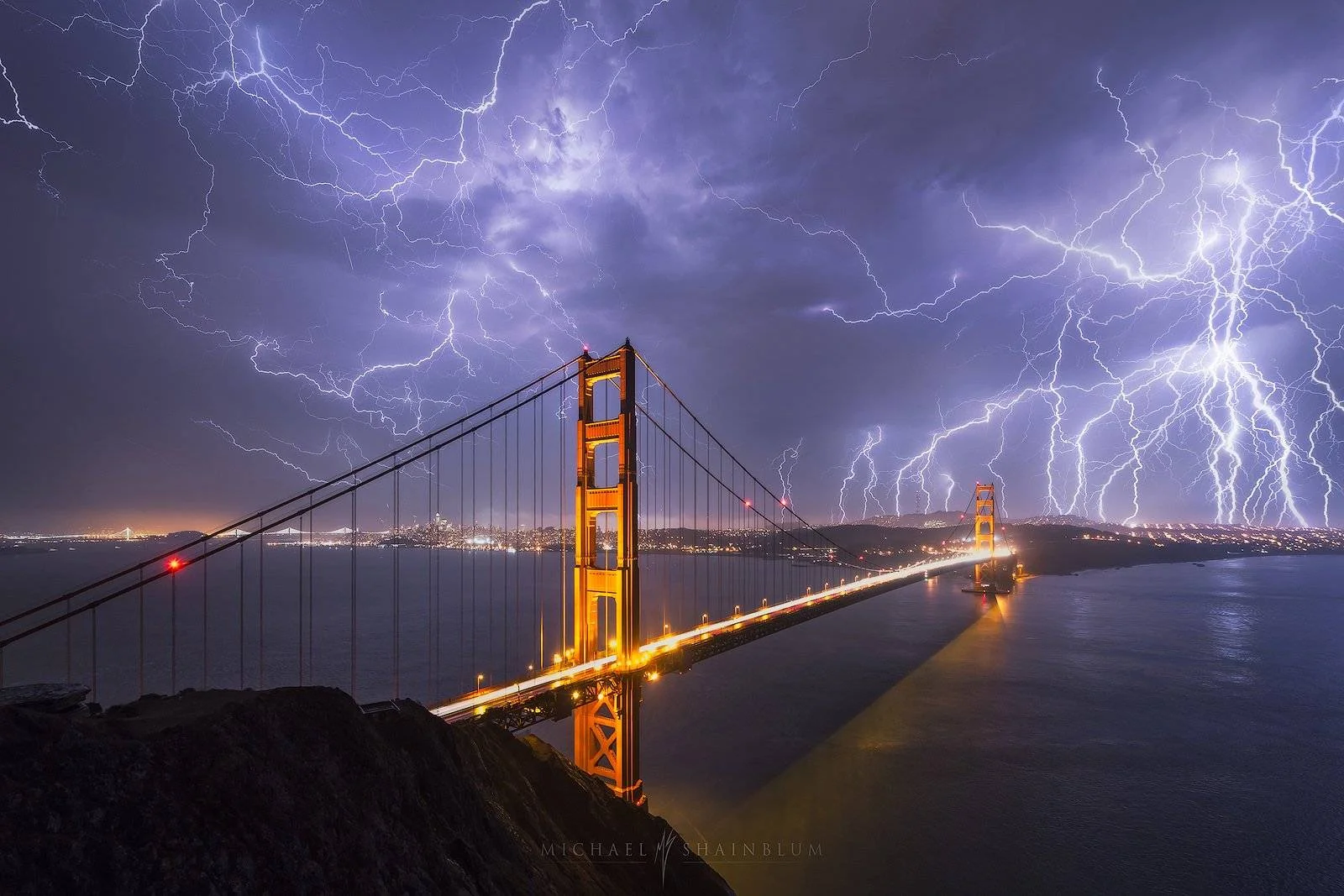 A truly amazing photograph taken by photographer Michael Shainblaum. This photograph shows the bridge lit up at night or dusk. There is lightning everywhere in the background. The image is truly amazing.