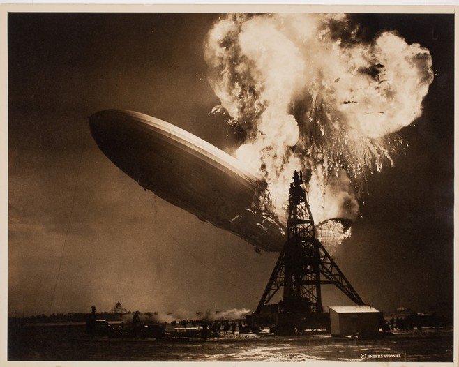 photograph shows the German airship LZ 129 Hindenburg engulfed in flames while attempting to dock at Naval Air Station Lakehurst, New Jersey. Shere's quick reflexes and precise timing immortalized the catastrophic moment. The image, taken with a handheld camera, conveys the scale and intensity of the disaster. The Hindenburg, filled with hydrogen, caught fire due to a spark, leading to 36 fatalities and marking the end of the airship era.