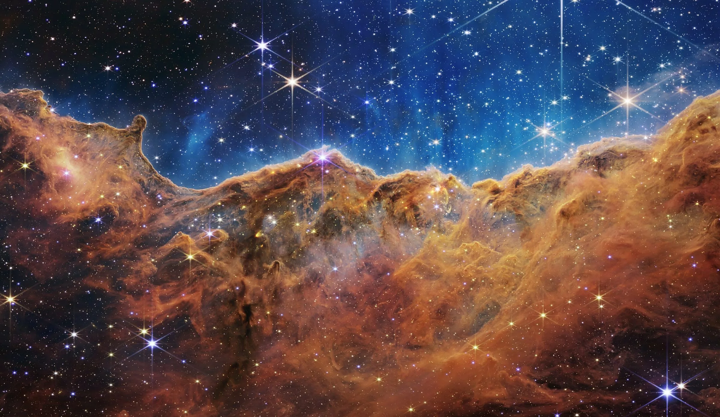 Image shows the Carina Nebula. It looks marvelous. There are many starts and galaxies, and a big glowing mountain of gas. It looks like some kind of psychedelic landscape.