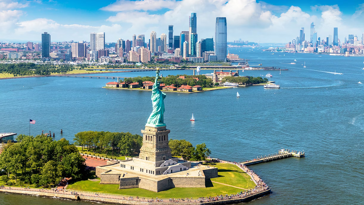 Photo taken from a helicopter. It shows the beautiful New York skyline, and in the foreground you can clearly see the Statue of Liberty on it's unique Liberty island.